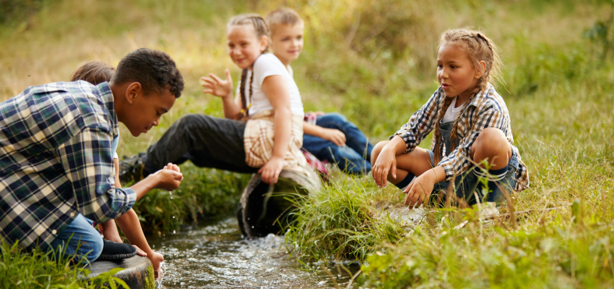 a group of children sitting on the side of a stream