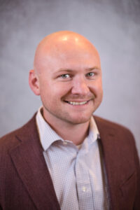 a man with a bald head wearing a brown jacket